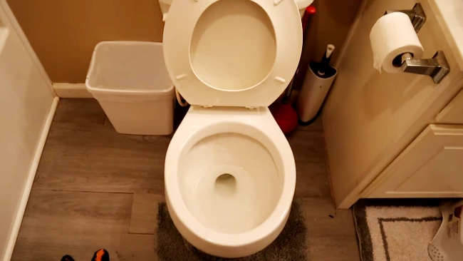 Why should I lower the water level in the toilet bowl before cleaning